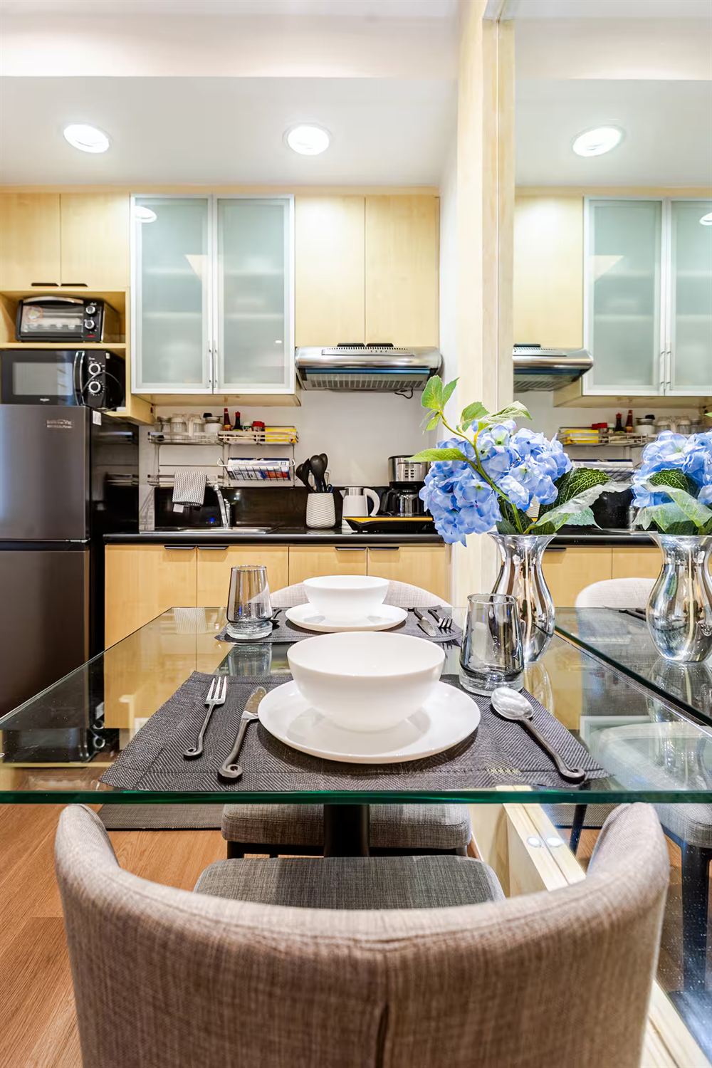 The glass dining table laid with white bowls, grey placemats and blue hydrangeas