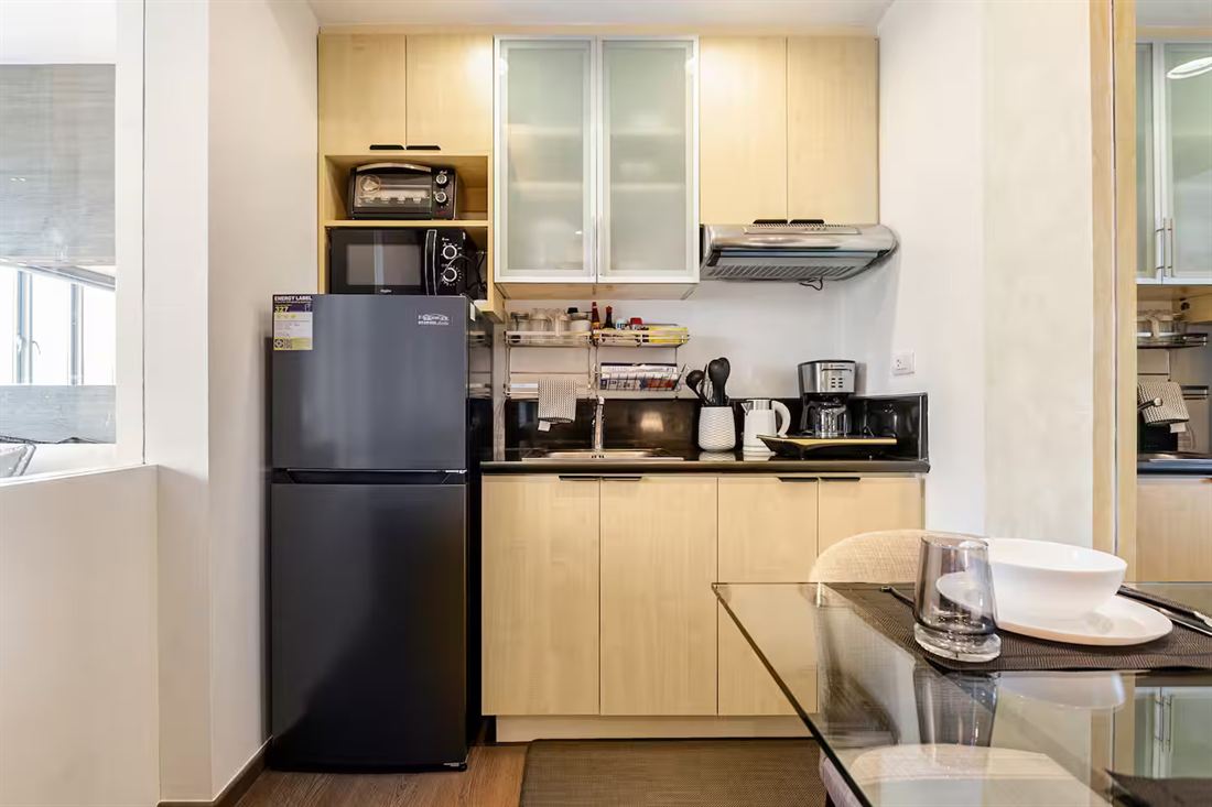 Galley kitchen with pale maple cabinets, a black fridge, oven toaster and coffee maker