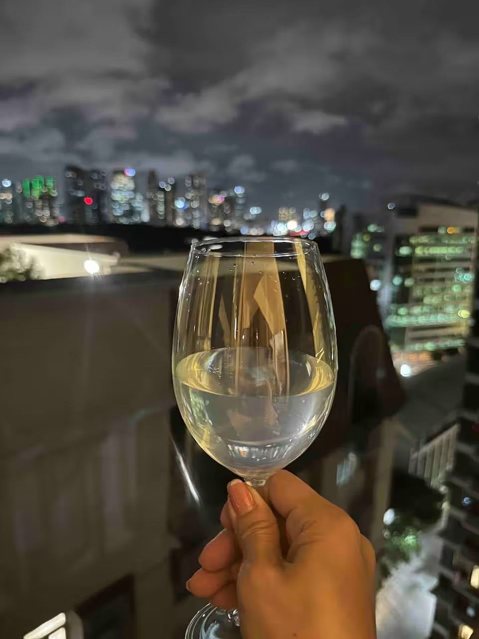 A glass of white wine held up against the city lights at night